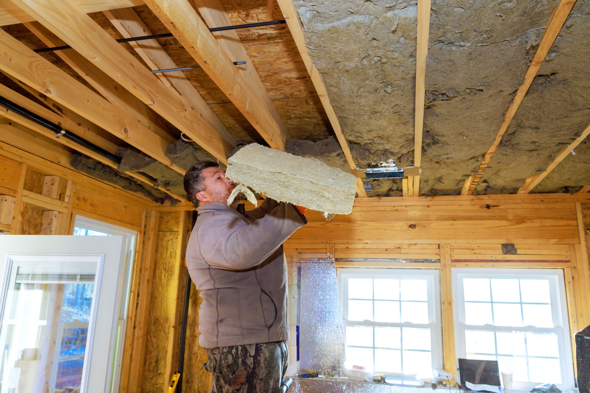 Worker installs insulation material in a wooden house during construction on a winter day